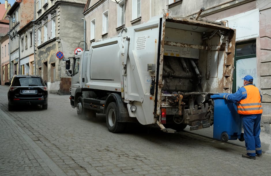 The image displays a neat pile of waste materials and debris situated outdoors, positioned on a concrete driveway or paved surface. In the foreground, there is a collection of large, irregularly shape